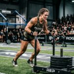 Atleta feminina empurra um trenó com pesos durante uma competição de fitness num pavilhão com público