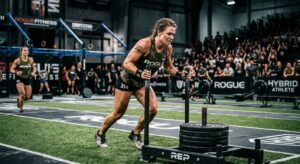Atleta feminina empurra um trenó com pesos durante uma competição de fitness num pavilhão com público